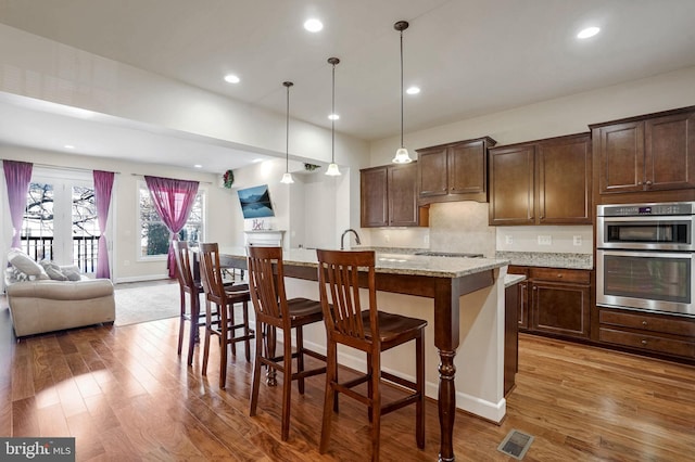 kitchen featuring a kitchen bar, light stone countertops, pendant lighting, and a kitchen island with sink