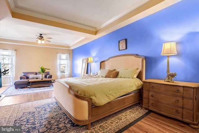 bedroom with ceiling fan, wood-type flooring, a tray ceiling, and crown molding