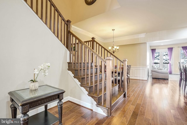 staircase with wood-type flooring, a notable chandelier, and ornamental molding