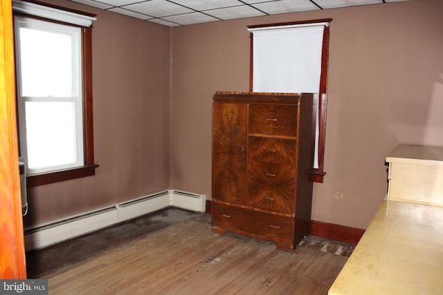 unfurnished room with baseboard heating, a paneled ceiling, and wood-type flooring