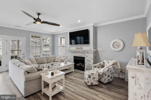 living room with light wood-type flooring, ceiling fan, crown molding, and a stone fireplace