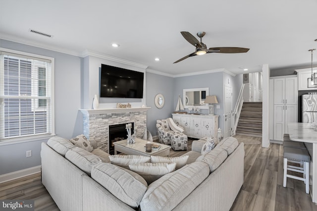 living room featuring crown molding, ceiling fan, dark wood-type flooring, and a stone fireplace