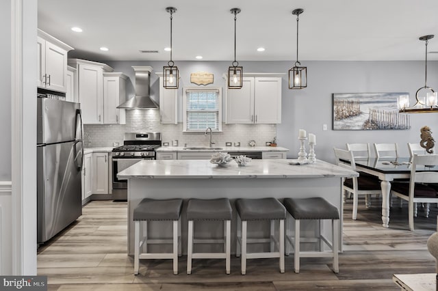 kitchen with hanging light fixtures, appliances with stainless steel finishes, wall chimney range hood, and white cabinetry