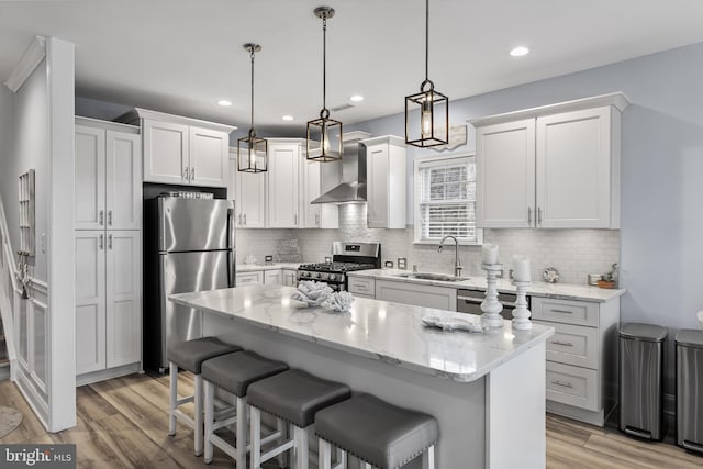 kitchen featuring appliances with stainless steel finishes, sink, wall chimney range hood, white cabinets, and a center island