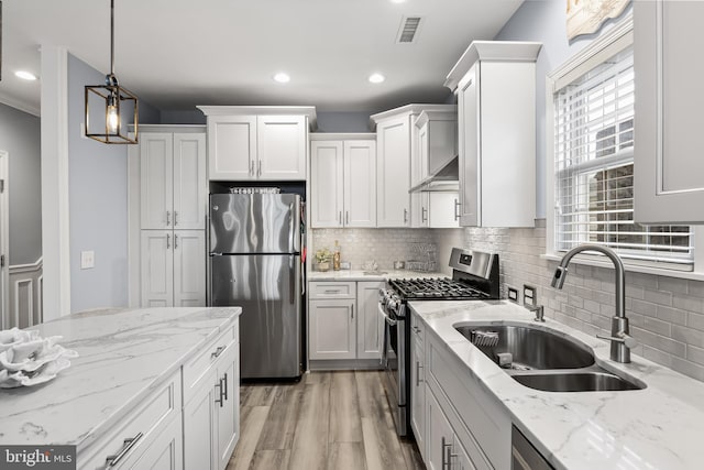 kitchen featuring light stone countertops, appliances with stainless steel finishes, decorative light fixtures, white cabinetry, and sink