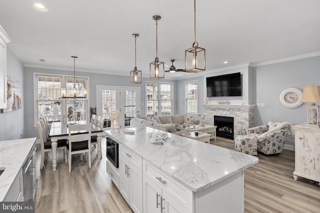 kitchen with white cabinetry, decorative light fixtures, a fireplace, light stone counters, and a center island