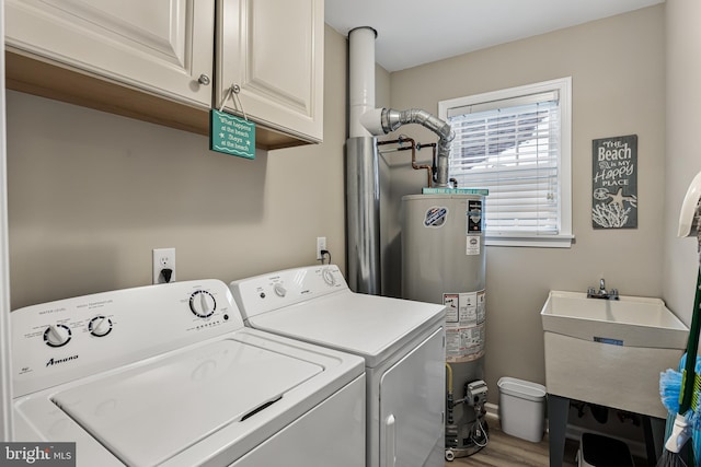 laundry room with water heater, hardwood / wood-style flooring, washing machine and dryer, cabinets, and sink