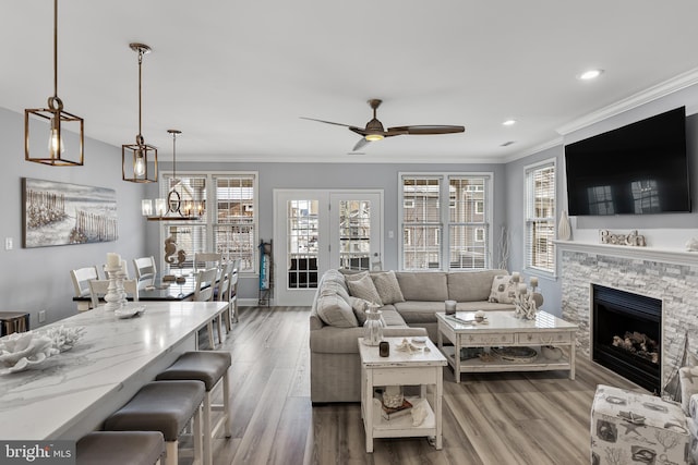 living room featuring ceiling fan, a stone fireplace, ornamental molding, and hardwood / wood-style flooring