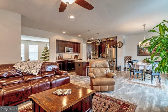 living room with light wood-type flooring, ceiling fan, and sink