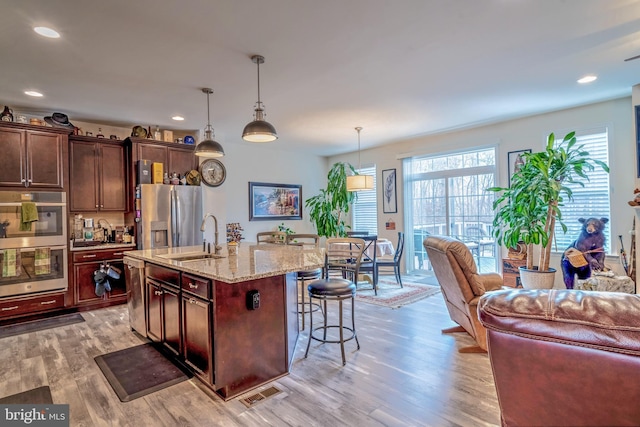 kitchen with a center island with sink, sink, hanging light fixtures, light wood-type flooring, and stainless steel appliances