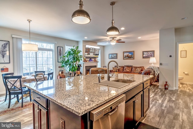 kitchen with stainless steel dishwasher, sink, hanging light fixtures, and a center island with sink