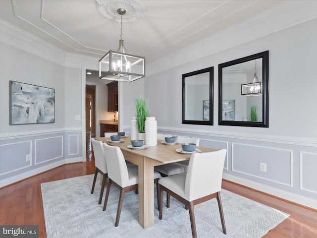 dining area with wood-type flooring, ornamental molding, and an inviting chandelier