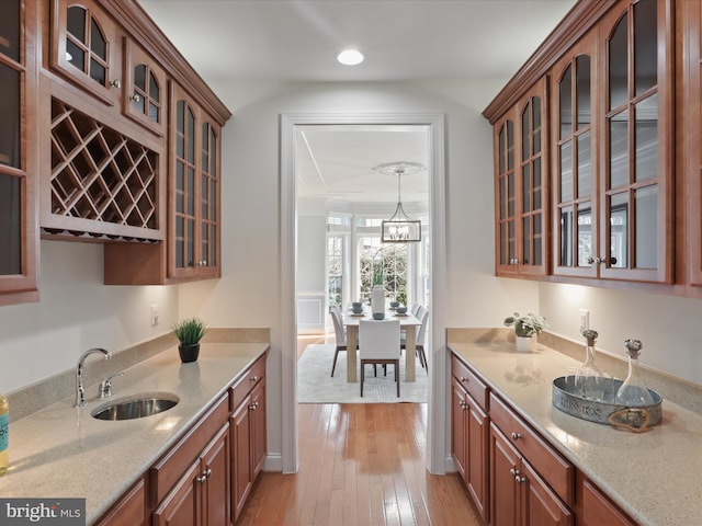 kitchen with hanging light fixtures, light hardwood / wood-style floors, sink, and light stone countertops