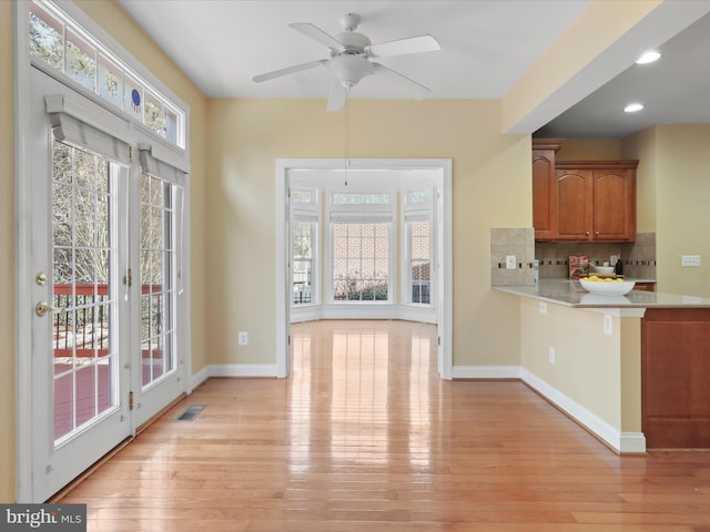 interior space featuring tasteful backsplash, ceiling fan, light wood-type flooring, and kitchen peninsula