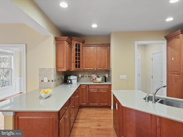 kitchen featuring light stone counters, sink, kitchen peninsula, and light wood-type flooring