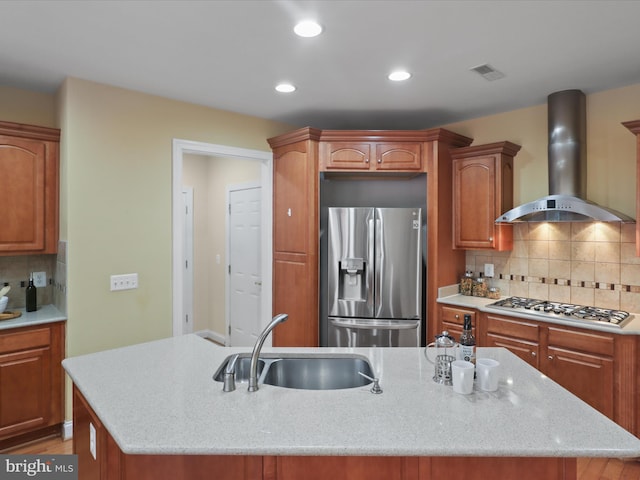 kitchen featuring sink, a center island with sink, wall chimney range hood, stainless steel appliances, and backsplash