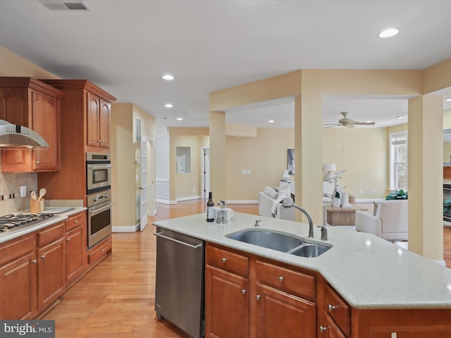 kitchen featuring appliances with stainless steel finishes, an island with sink, sink, backsplash, and light hardwood / wood-style floors