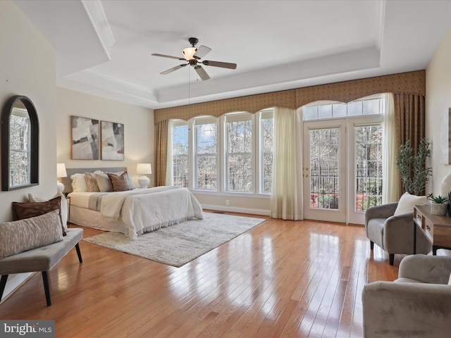 bedroom featuring a tray ceiling, access to outside, multiple windows, and light wood-type flooring