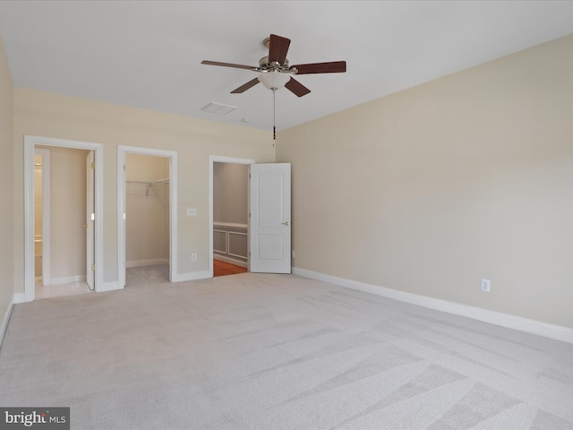 unfurnished bedroom with light carpet, a walk in closet, a closet, and ceiling fan