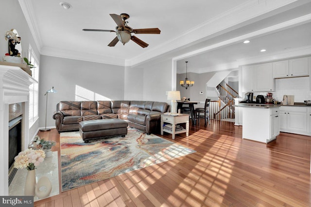 living room with crown molding, ceiling fan with notable chandelier, a high end fireplace, and light hardwood / wood-style flooring