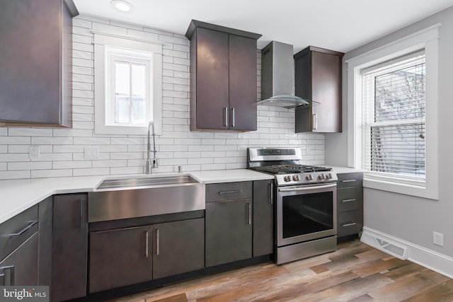 kitchen with dark brown cabinetry, sink, gas stove, light hardwood / wood-style flooring, and wall chimney range hood