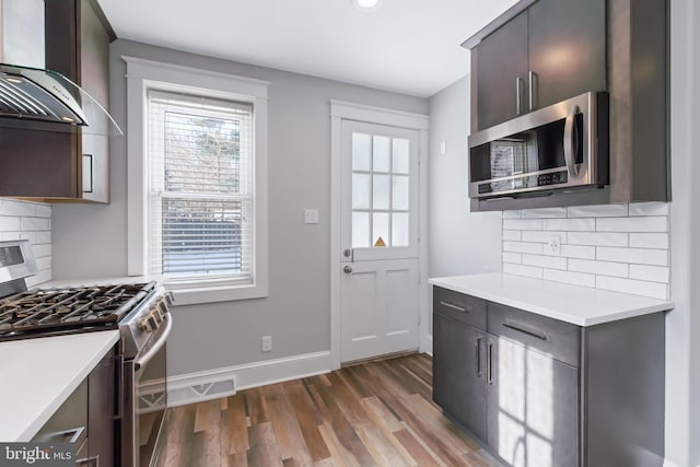 kitchen with dark brown cabinets, wall chimney exhaust hood, stainless steel appliances, and decorative backsplash