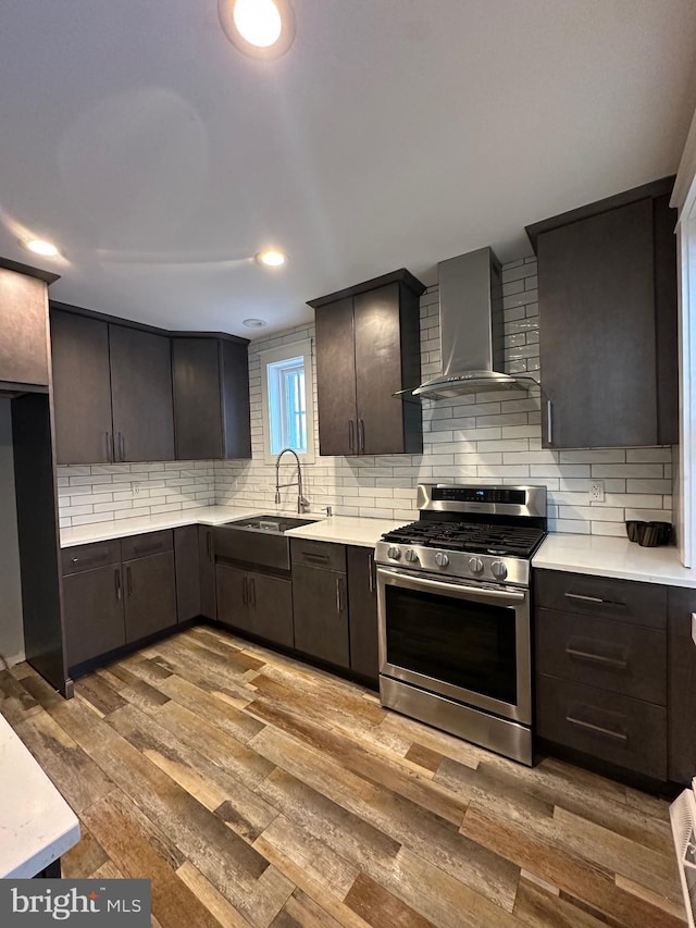 kitchen with sink, wood-type flooring, stainless steel range with gas cooktop, and wall chimney exhaust hood