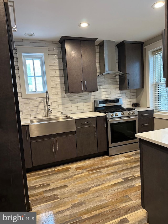 kitchen with sink, stainless steel gas range oven, decorative backsplash, wall chimney exhaust hood, and light wood-type flooring