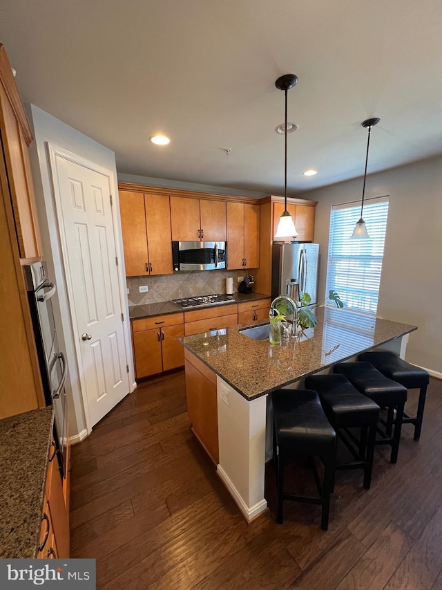 kitchen with appliances with stainless steel finishes, pendant lighting, an island with sink, sink, and a kitchen bar