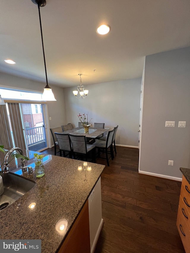 kitchen featuring dark hardwood / wood-style floors, sink, dark stone counters, hanging light fixtures, and an inviting chandelier