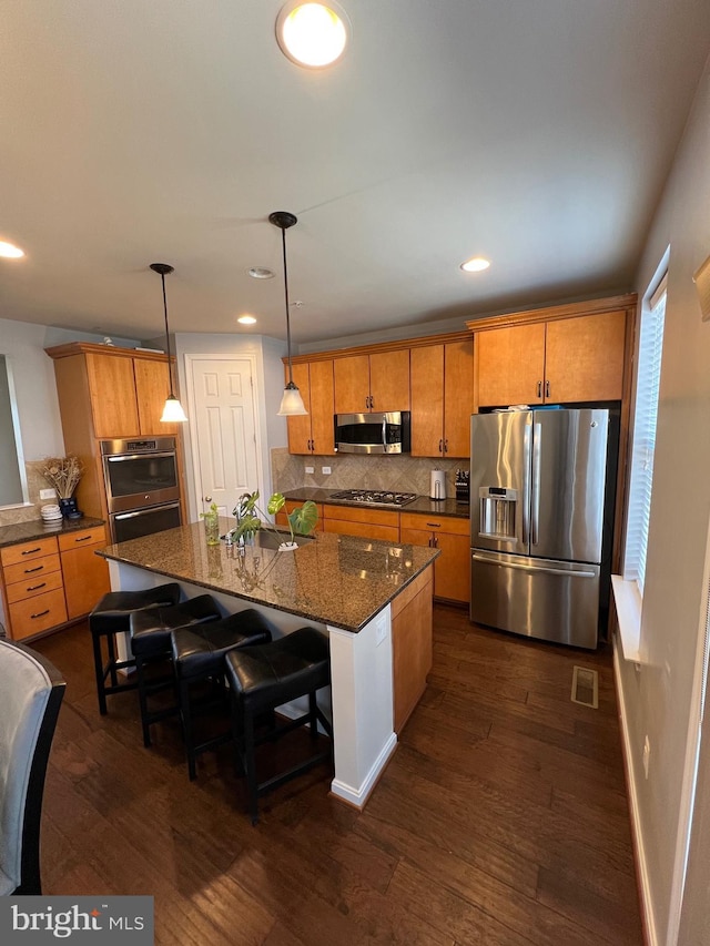 kitchen with an island with sink, appliances with stainless steel finishes, a breakfast bar, and pendant lighting