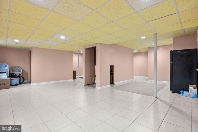 basement featuring black fridge, a paneled ceiling, and light tile patterned flooring