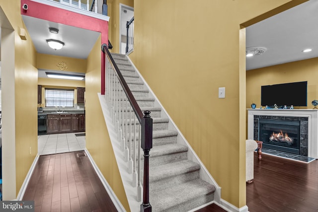 staircase featuring a tiled fireplace, sink, and hardwood / wood-style flooring