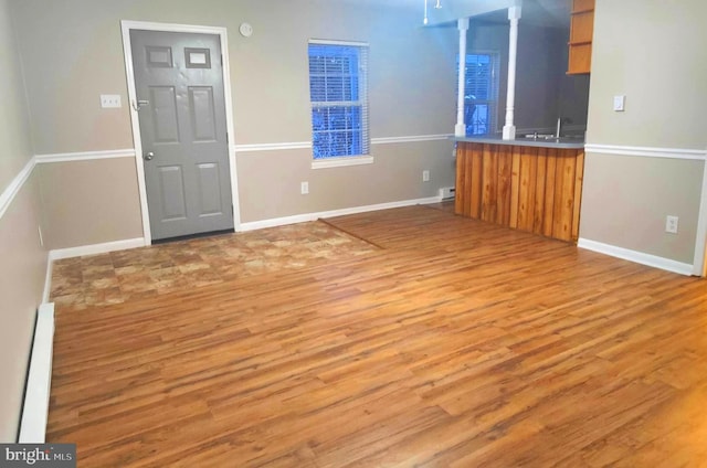 unfurnished living room featuring sink, hardwood / wood-style floors, and a baseboard heating unit