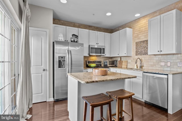 kitchen with a center island, white cabinetry, a breakfast bar area, stainless steel appliances, and light stone counters