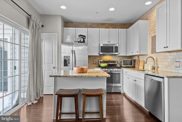 kitchen with light stone countertops, white cabinets, a kitchen island, stainless steel appliances, and sink