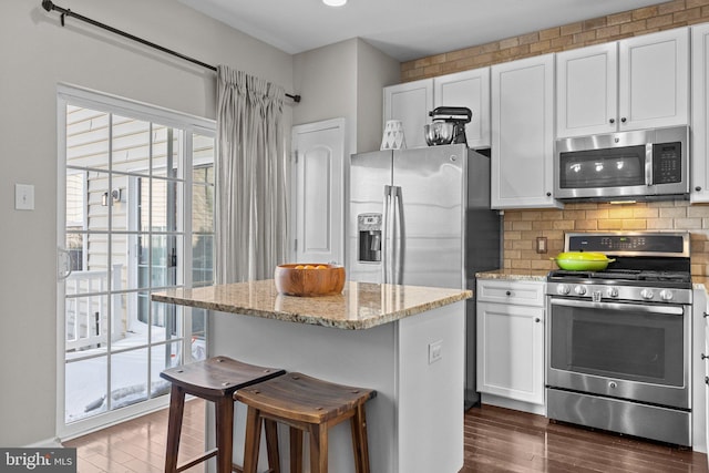 kitchen with decorative backsplash, a breakfast bar area, stainless steel appliances, white cabinets, and light stone counters