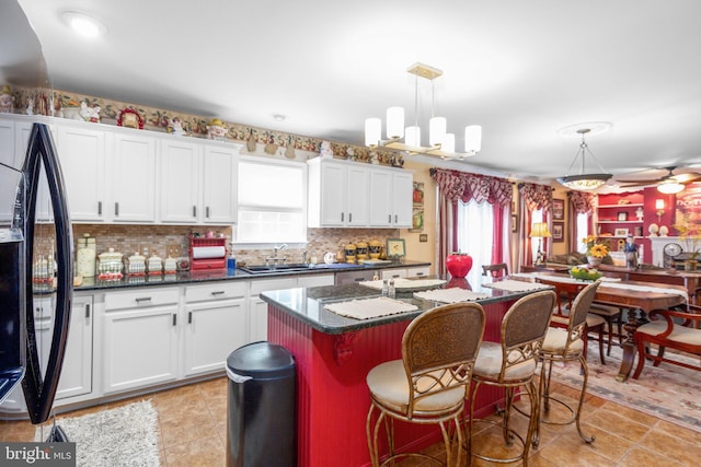 kitchen featuring decorative light fixtures, a kitchen island, sink, a breakfast bar area, and white cabinets