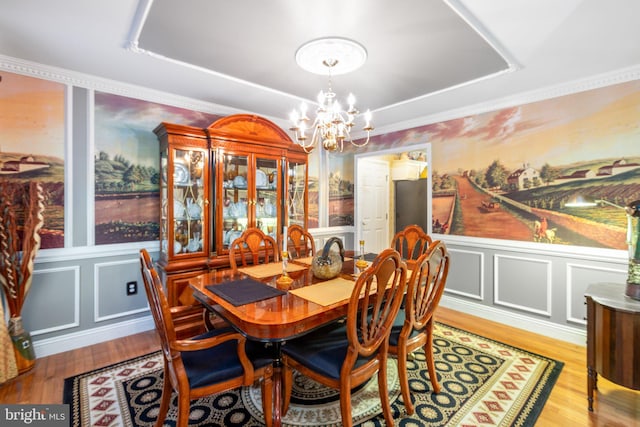 dining area with ornamental molding, a raised ceiling, hardwood / wood-style flooring, and a notable chandelier