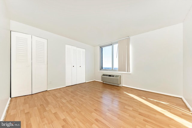 unfurnished bedroom featuring hardwood / wood-style floors, an AC wall unit, and two closets