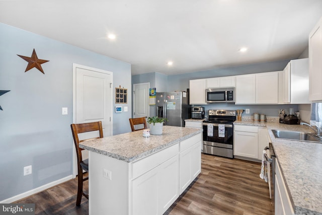 kitchen with white cabinetry, a kitchen bar, stainless steel appliances, a kitchen island, and sink