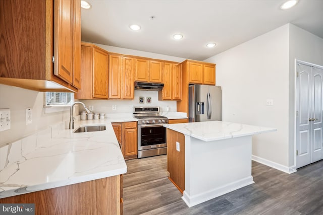 kitchen with a center island, sink, dark wood-type flooring, light stone countertops, and stainless steel appliances