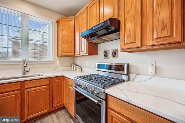 kitchen with gas stove, light wood-type flooring, light stone countertops, range hood, and sink