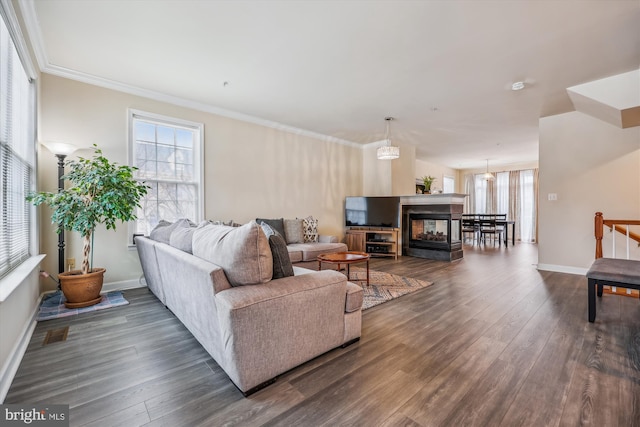 living room with a healthy amount of sunlight, dark wood-type flooring, a multi sided fireplace, and ornamental molding