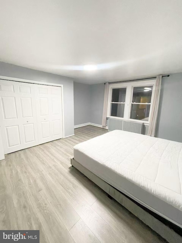 unfurnished bedroom with radiator heating unit, light hardwood / wood-style flooring, and a closet