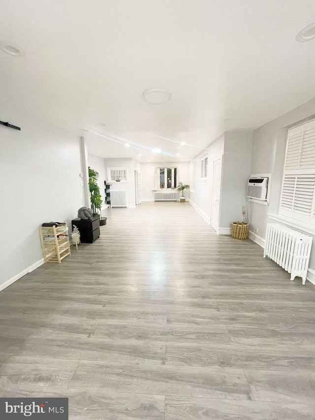 unfurnished living room with a wall unit AC, light wood-type flooring, and radiator heating unit