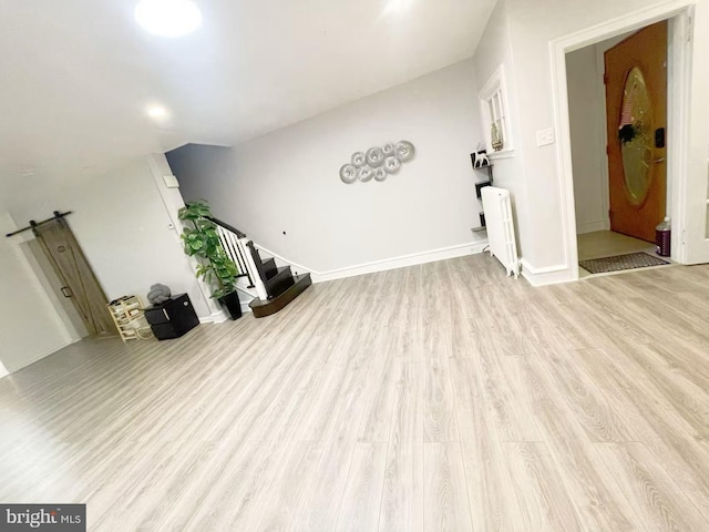 unfurnished living room featuring a barn door, light hardwood / wood-style floors, and radiator heating unit