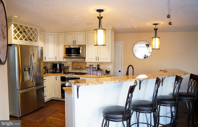 kitchen featuring light stone counters, dark wood-type flooring, a breakfast bar, appliances with stainless steel finishes, and backsplash