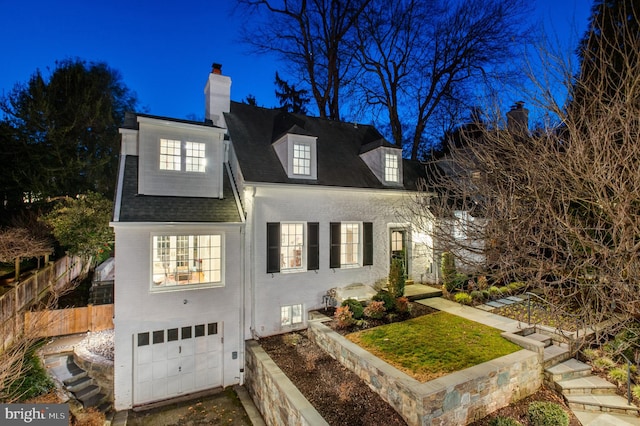 view of front of house featuring brick siding, roof with shingles, a chimney, an attached garage, and fence