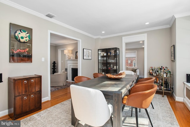 dining room with a fireplace, light wood finished floors, visible vents, ornamental molding, and baseboards